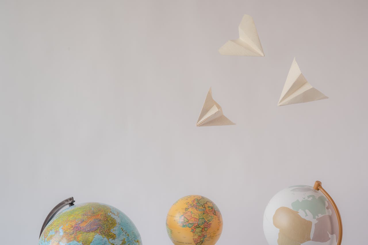 who-we-are Paper airplanes fly over colorful globes, symbolizing travel and exploration on a white background.